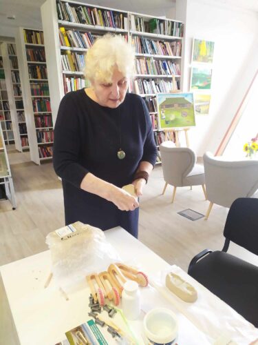 Vyresnio amžiaus moteris bibliotekoje moko keramikos meno įpatybių.