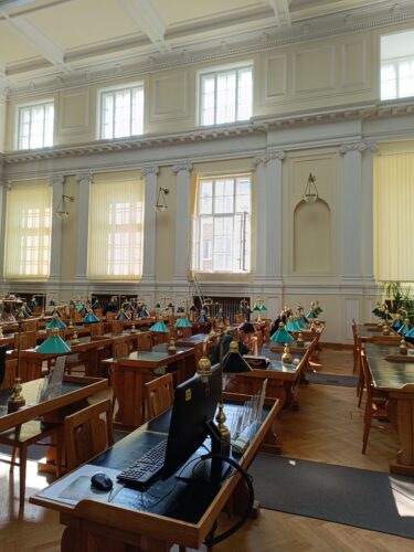 Bibliotekos erdvė. Klasicistinė erdvi salė. Žali šviestuvai. Rudi senoviniai stalai.